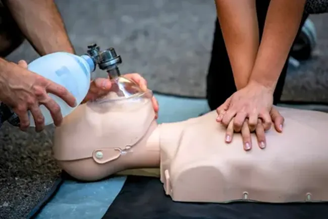 CPR instructor observing students practicing rescue breaths using barrier masks on mannequins