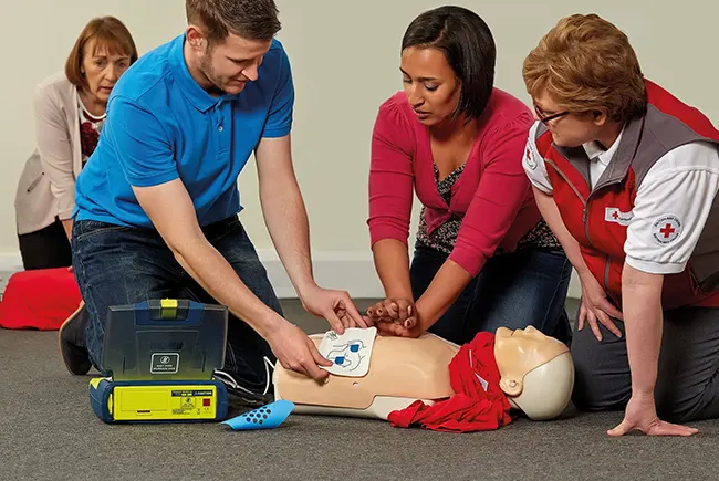 Close-up of hands operating AED device beside mannequin on training mat
